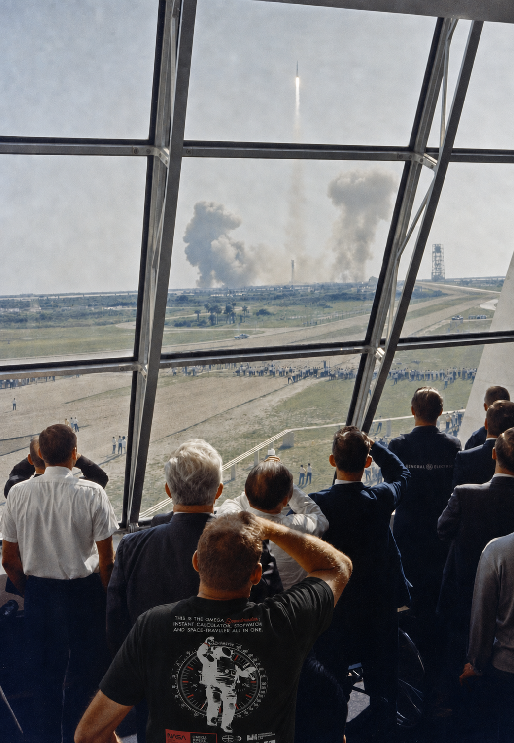 Crowd watching a rocket launch through a glass observation window